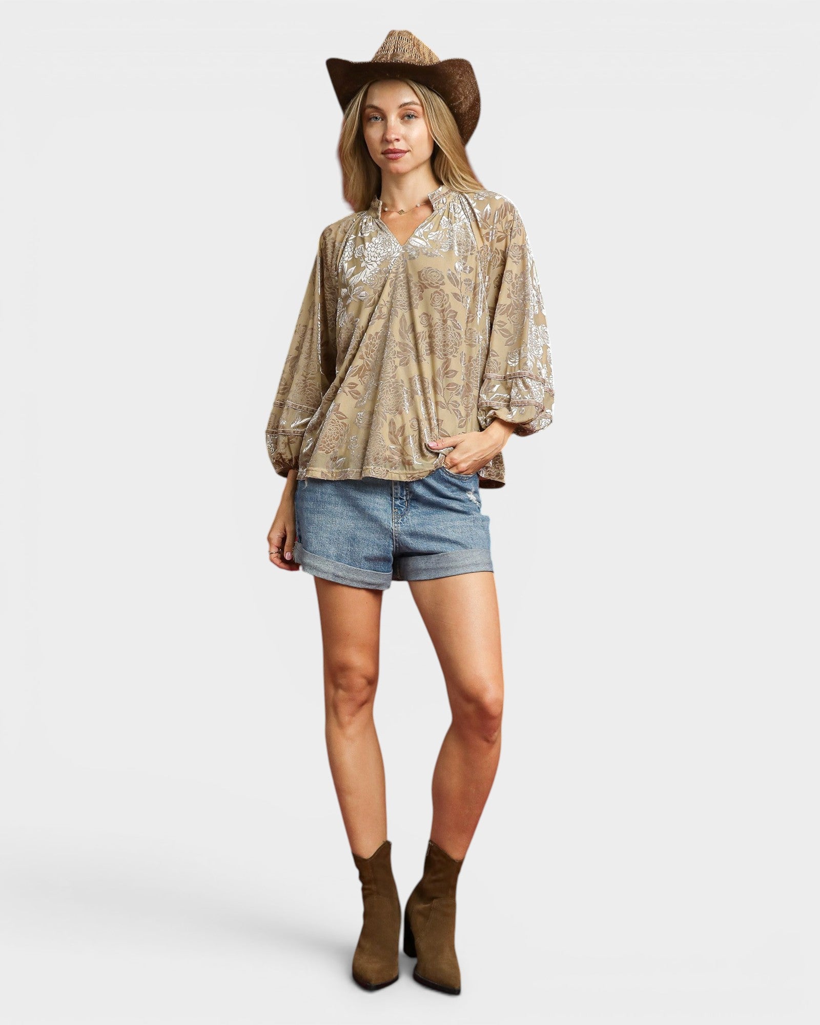 Woman wearing a patterned blouse, denim shorts, and a cowboy hat on a white background