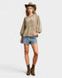 Woman wearing a patterned blouse, denim shorts, and a cowboy hat on a white background