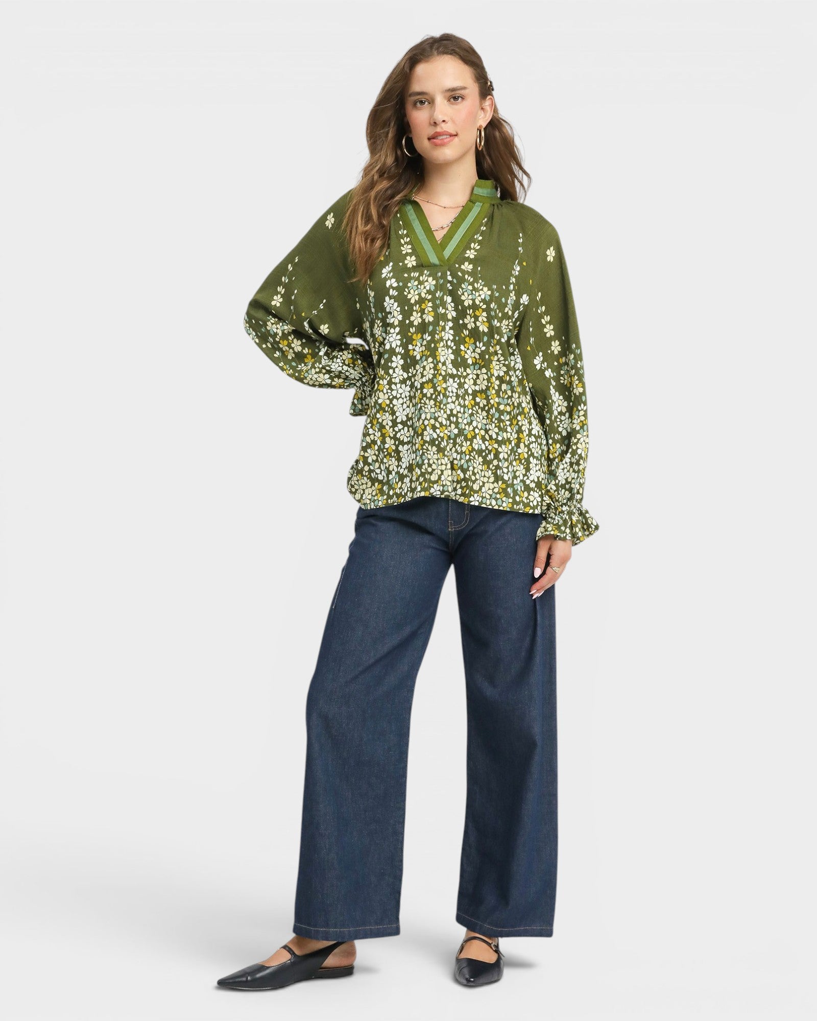 Woman wearing a green floral blouse and blue jeans on a white background