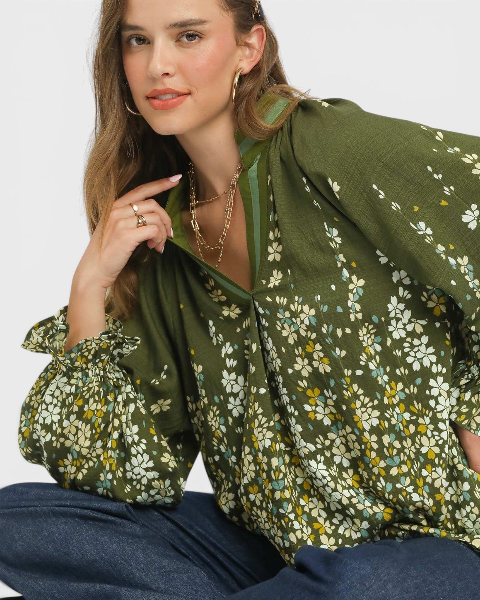 Woman wearing a green floral blouse sitting on a white background