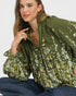 Woman wearing a green floral blouse sitting on a white background