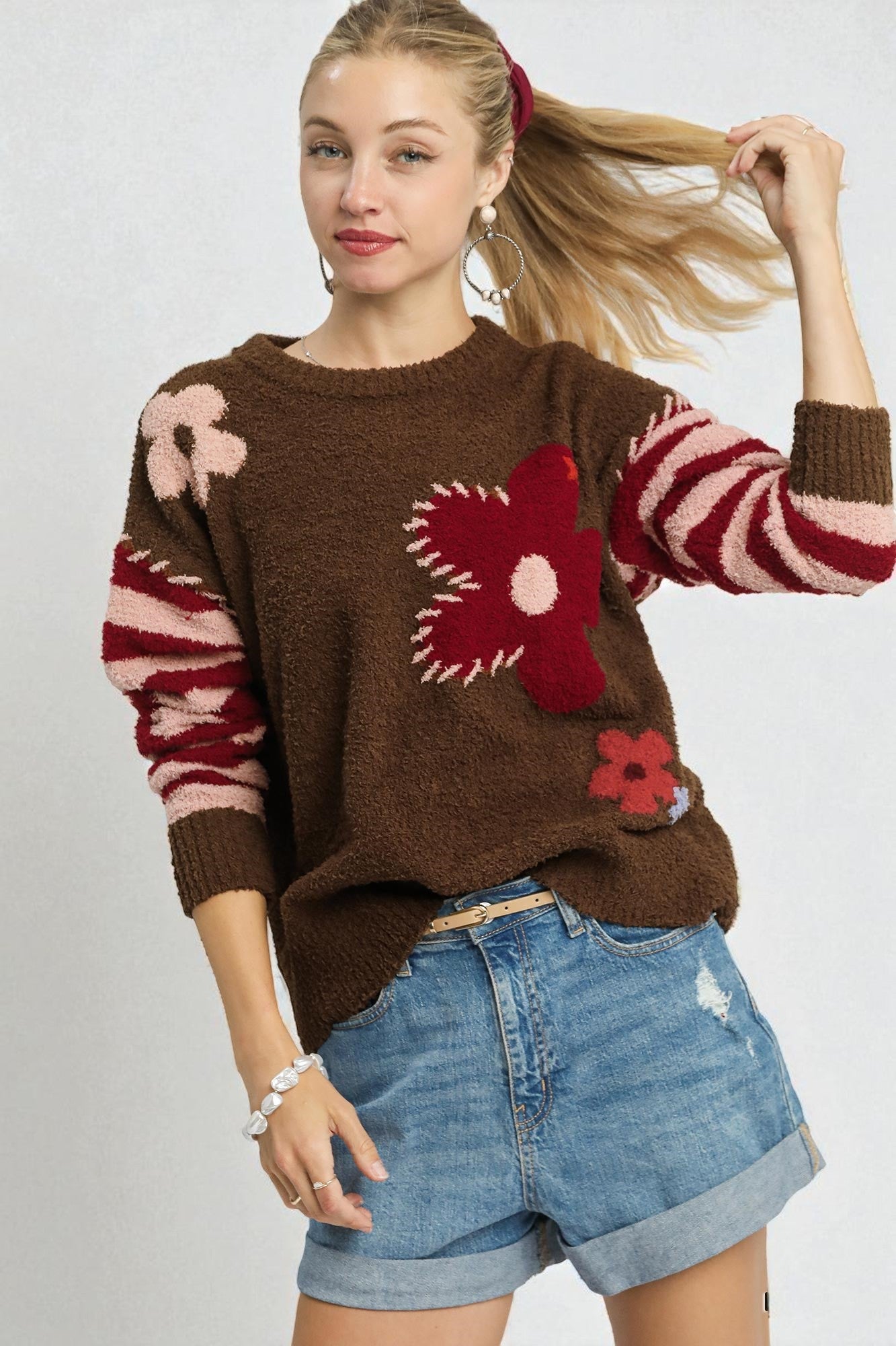 Woman wearing a brown sweater with floral patterns and denim shorts on a white background
