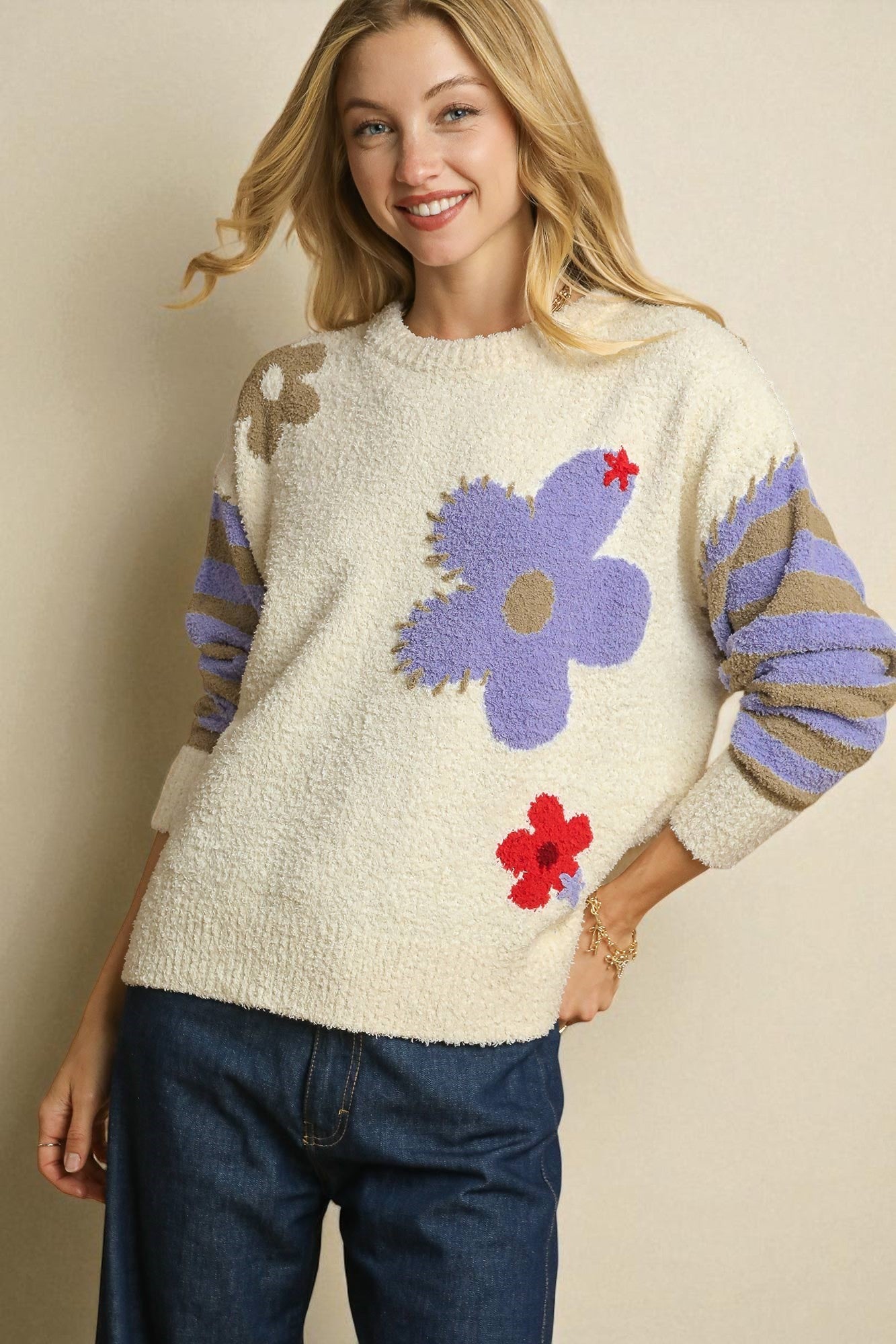 Woman wearing a cream sweater with colorful floral patterns on a beige background