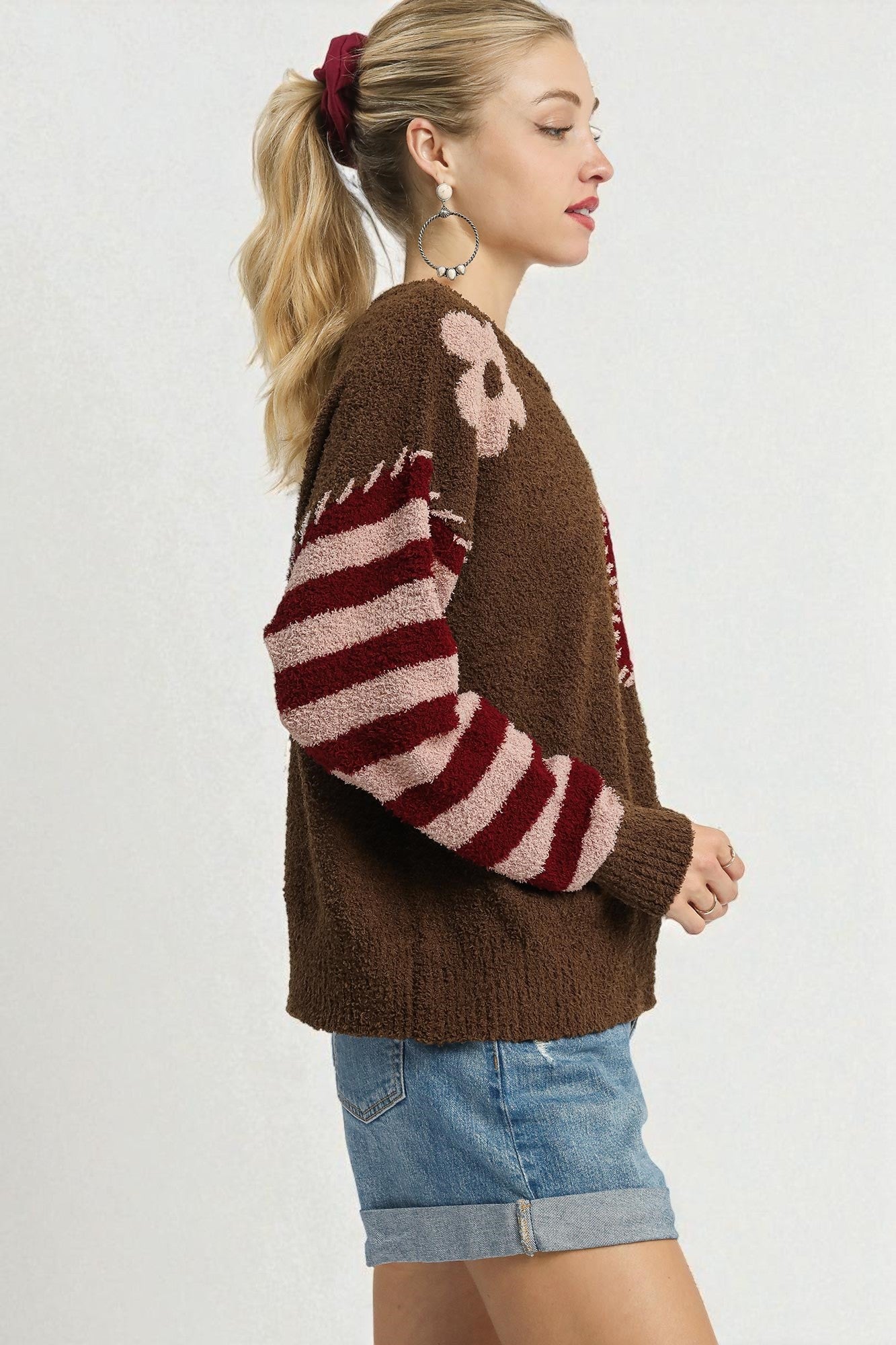 Woman wearing a brown sweater with striped sleeves and denim shorts on a white background