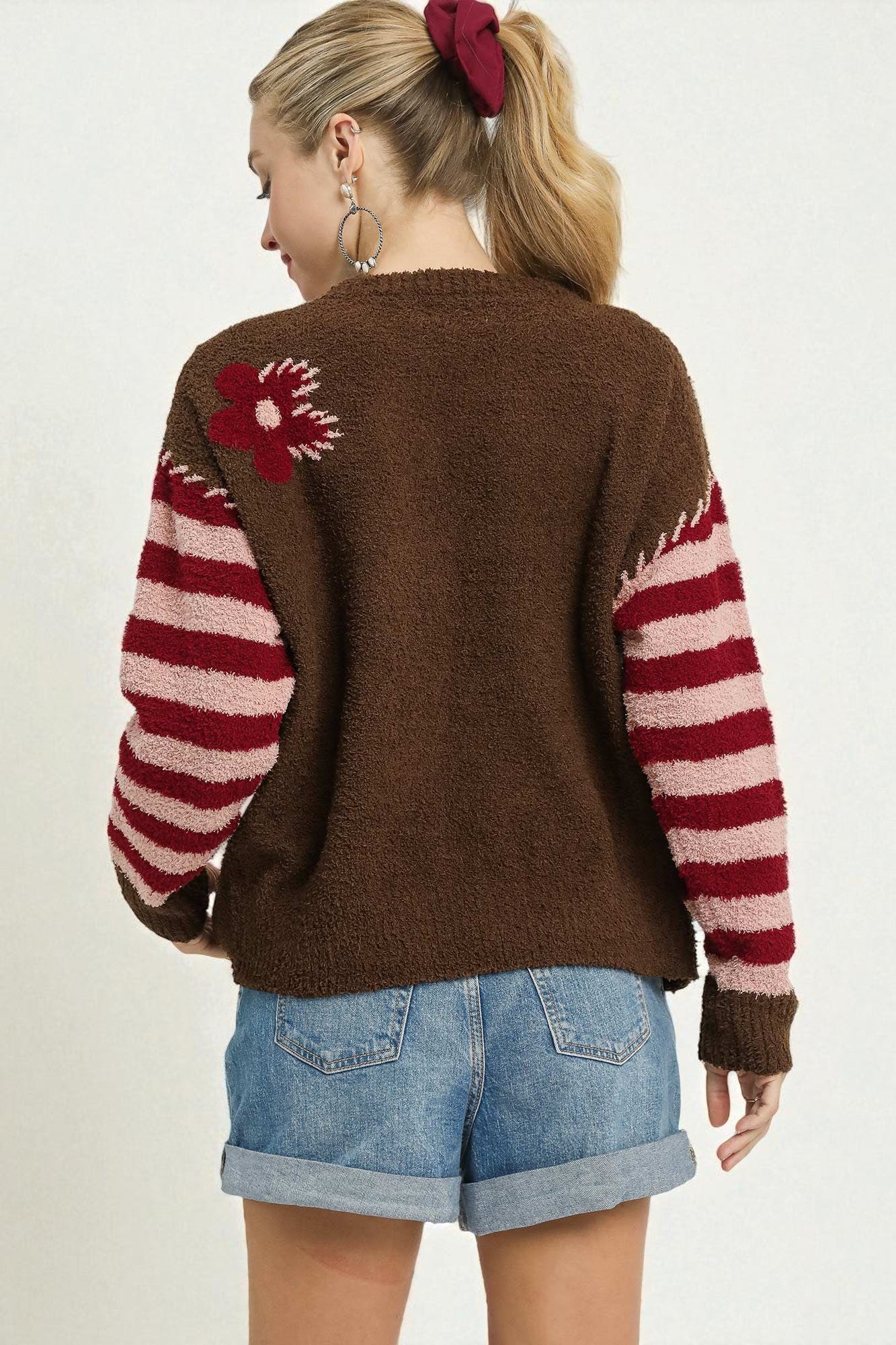 Person wearing a brown sweater with red and white pattern, standing against a plain background