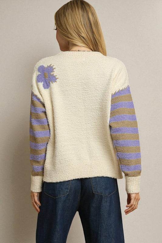Person wearing a cream sweater with purple and brown stripes and a floral design on the back, against a beige background.