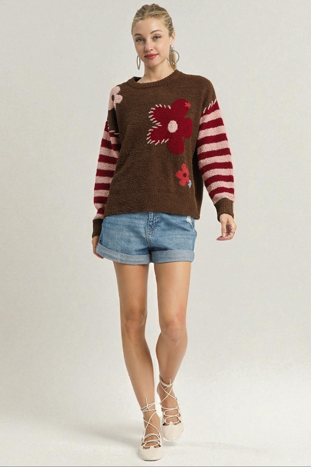 Woman wearing a brown sweater with floral designs and denim shorts on a white background