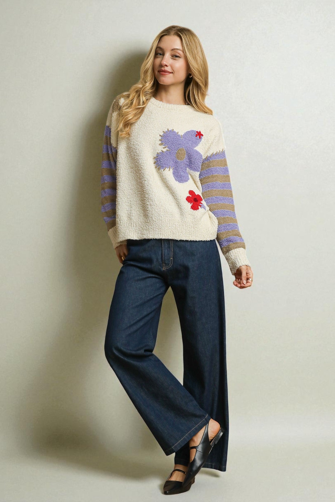 Woman wearing a sweater with a colorful design and blue jeans against a plain background
