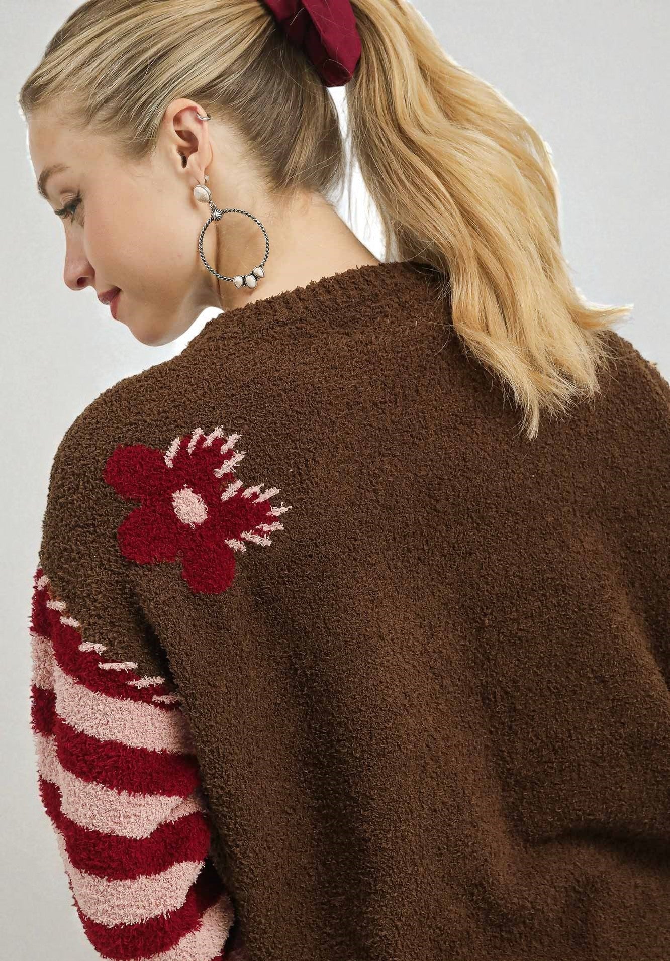 Woman wearing a brown cardigan with red and white patterned sleeves and a flower design on the back.