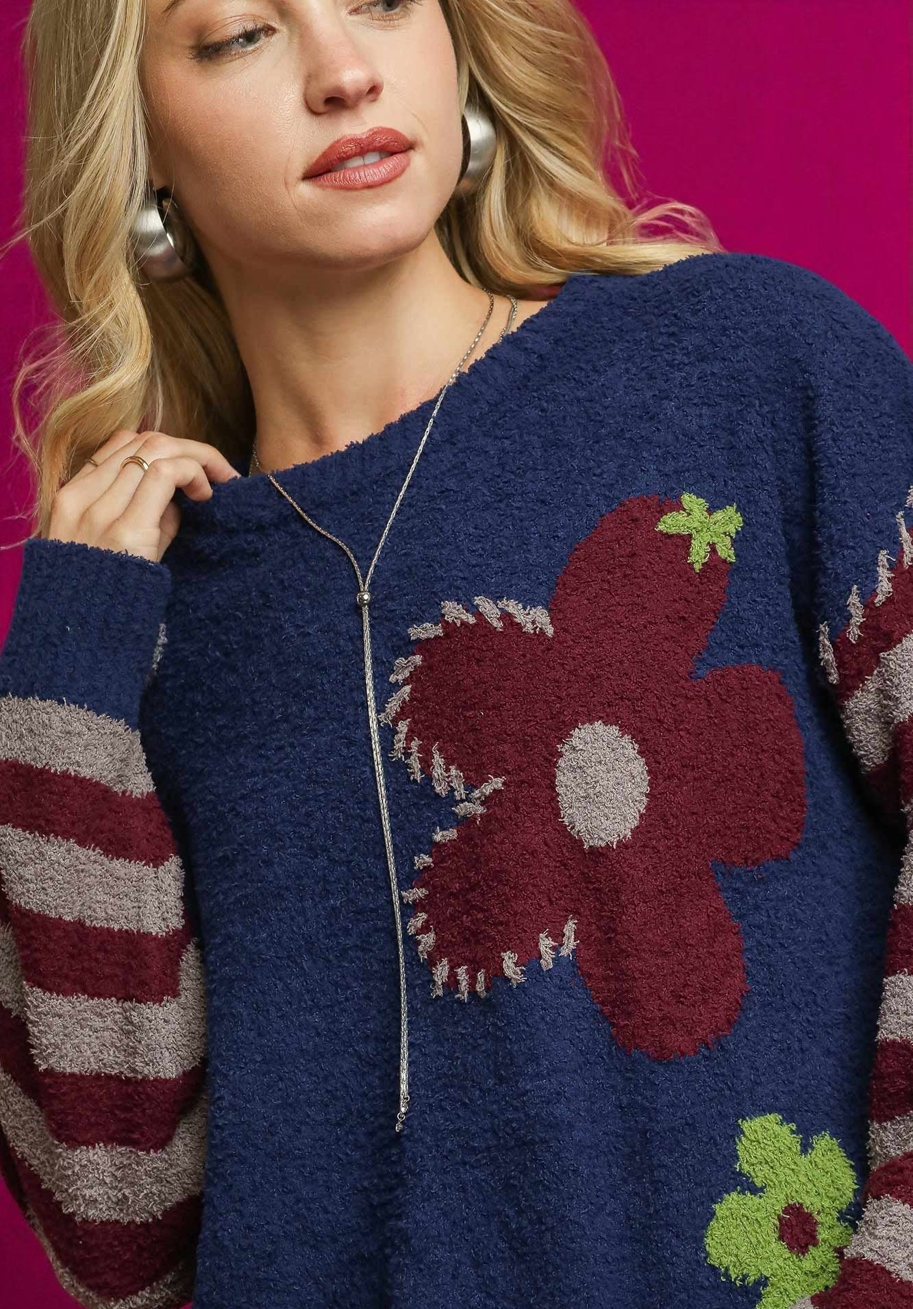 Woman wearing a blue sweater with a floral design on a pink background