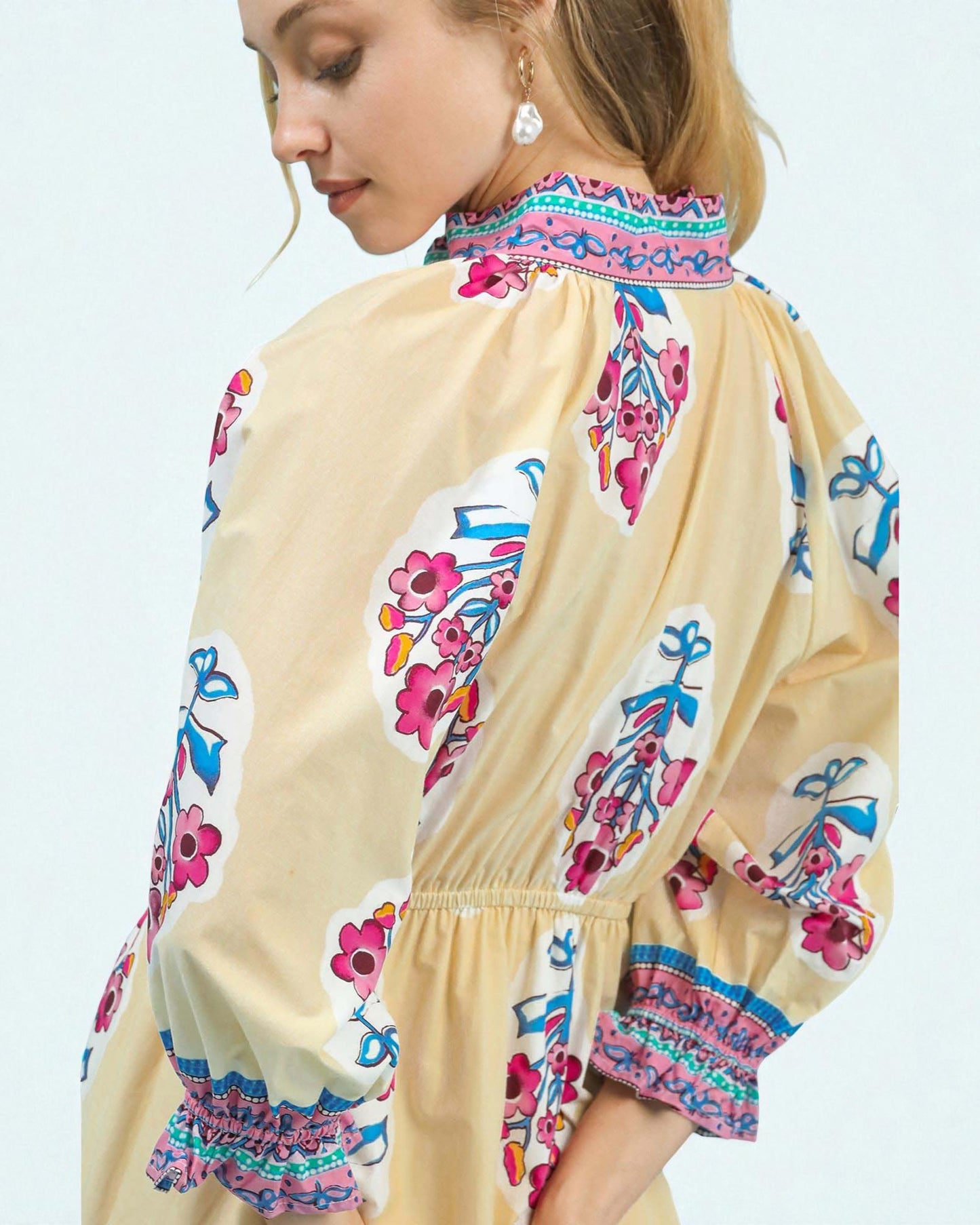 Woman wearing a beige dress with colorful floral embroidery on a light blue background