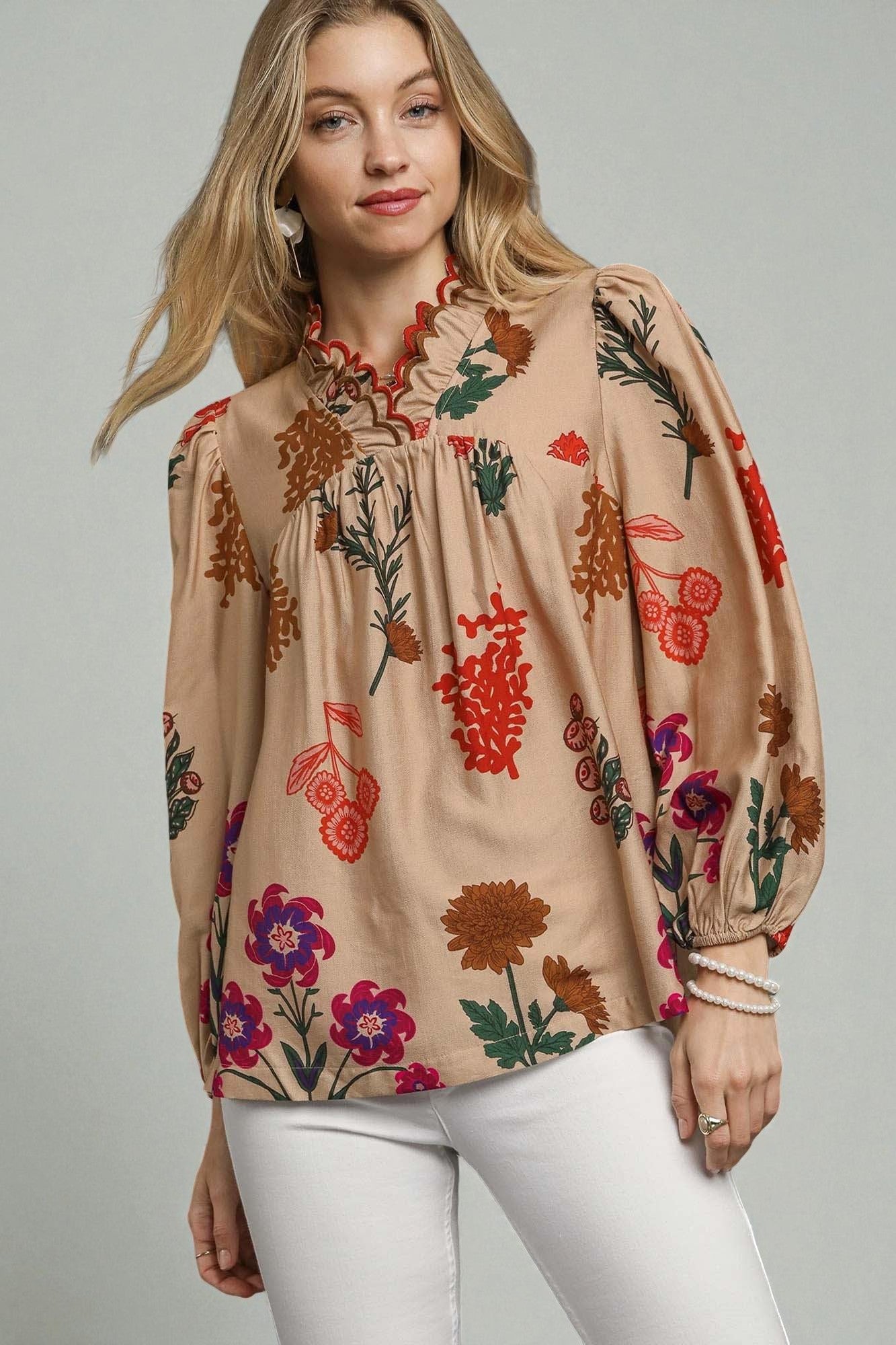 Woman wearing a beige blouse with colorful floral patterns on a plain background