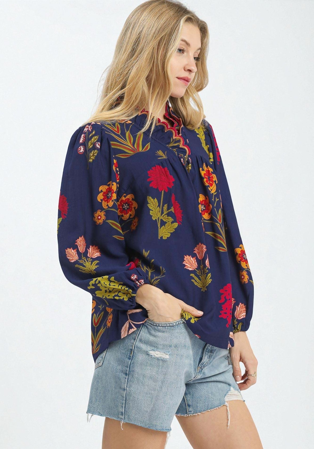 Woman wearing a navy floral blouse with denim shorts on a white background