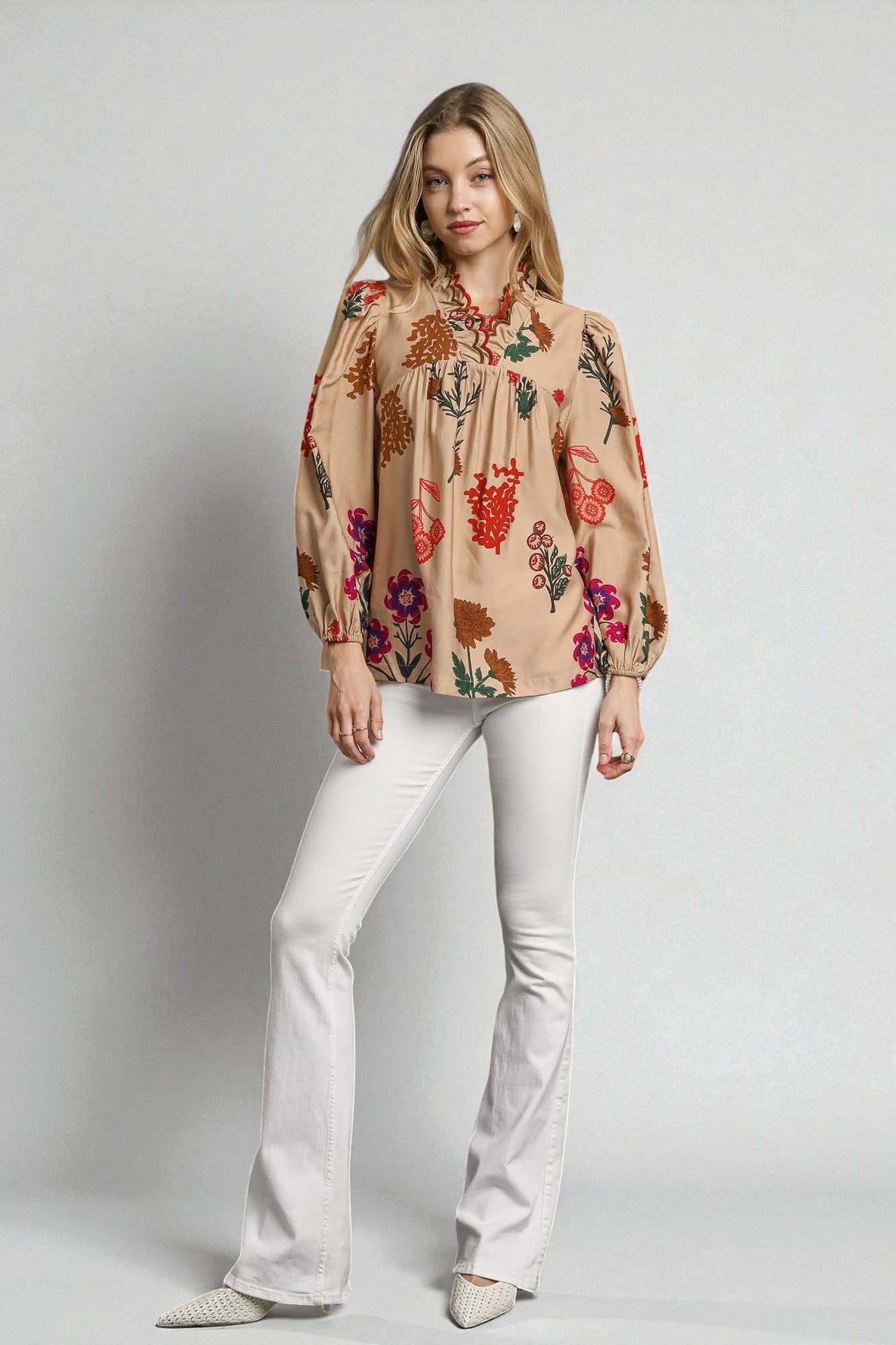 Woman wearing a floral blouse and white pants on a plain background