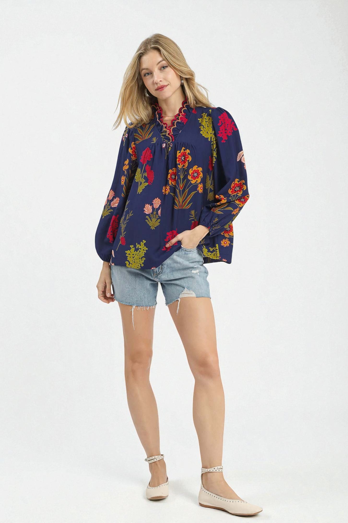 Woman wearing a colorful floral blouse and denim shorts on a white background