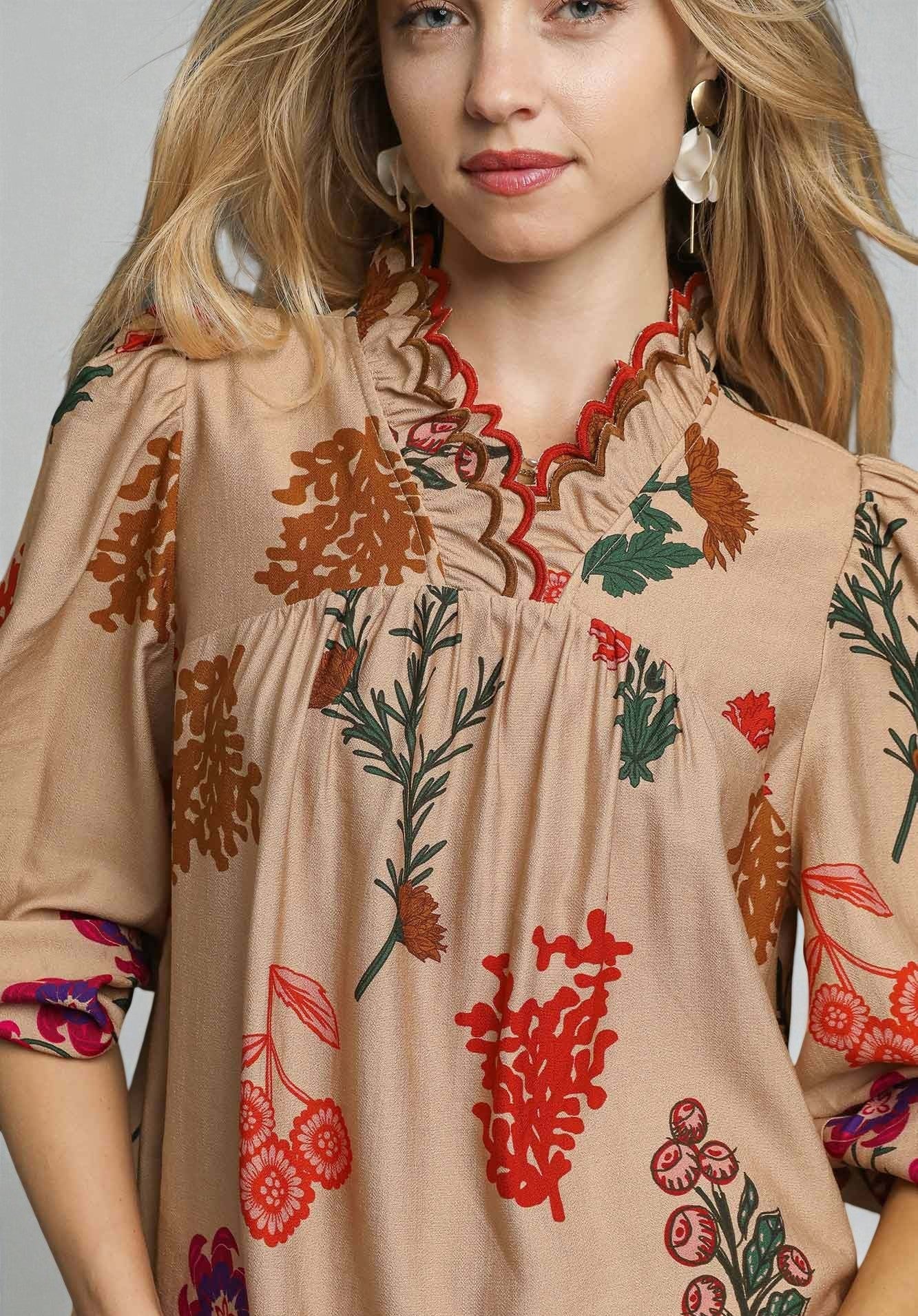Woman wearing a beige dress with colorful floral embroidery on a plain background