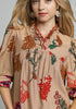 Woman wearing a beige dress with colorful floral embroidery on a plain background