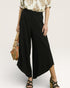 Person wearing black wide-leg pants with a beige top and holding a straw bag on a plain background