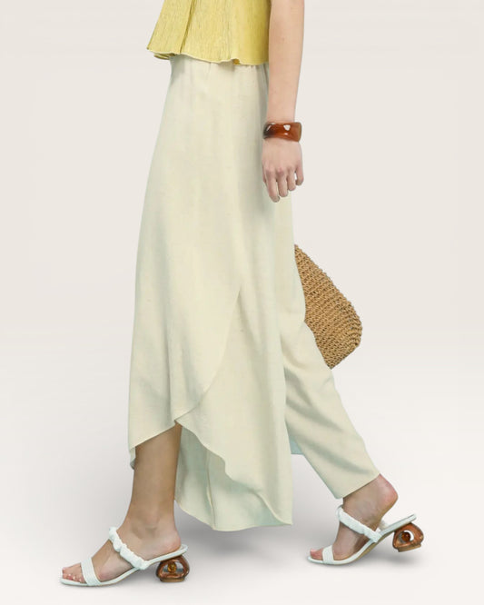 Person wearing a yellow top and light green skirt holding a woven bag on a plain background