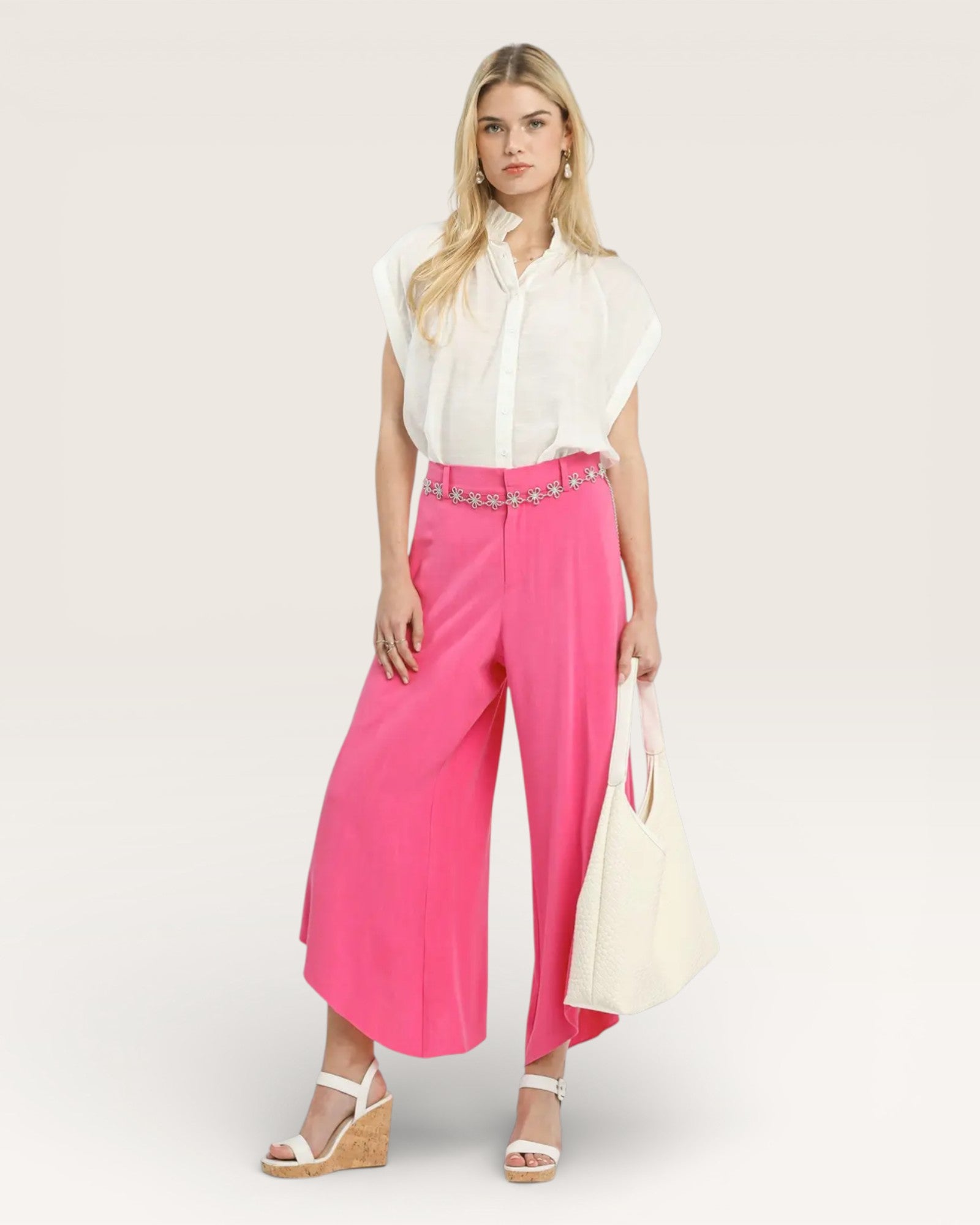 Woman wearing a white blouse and bright pink pants with a belt on a white background