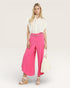 Woman wearing a white blouse and bright pink pants with a belt on a white background