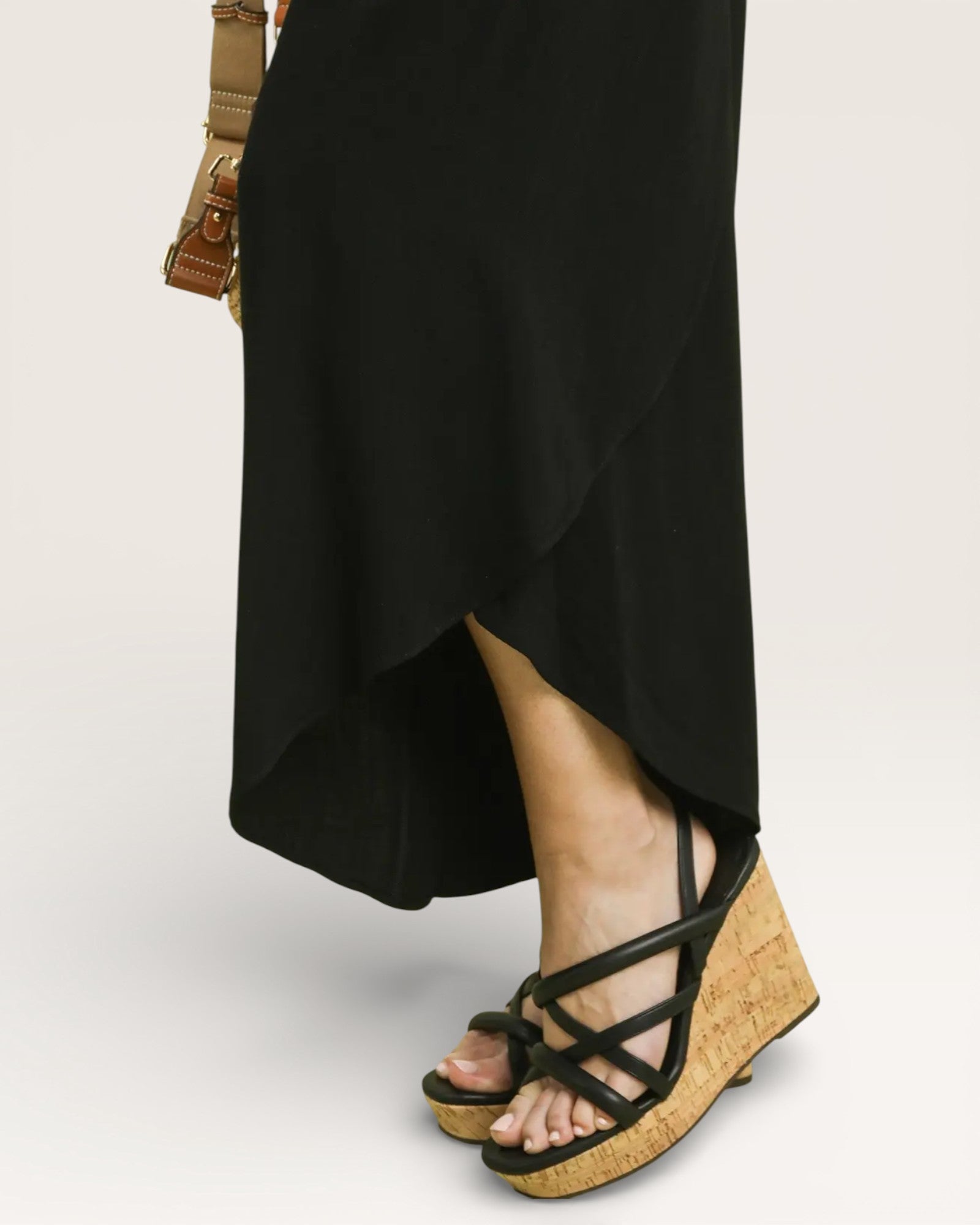 Person wearing black sandals with cork wedge sole on a plain background