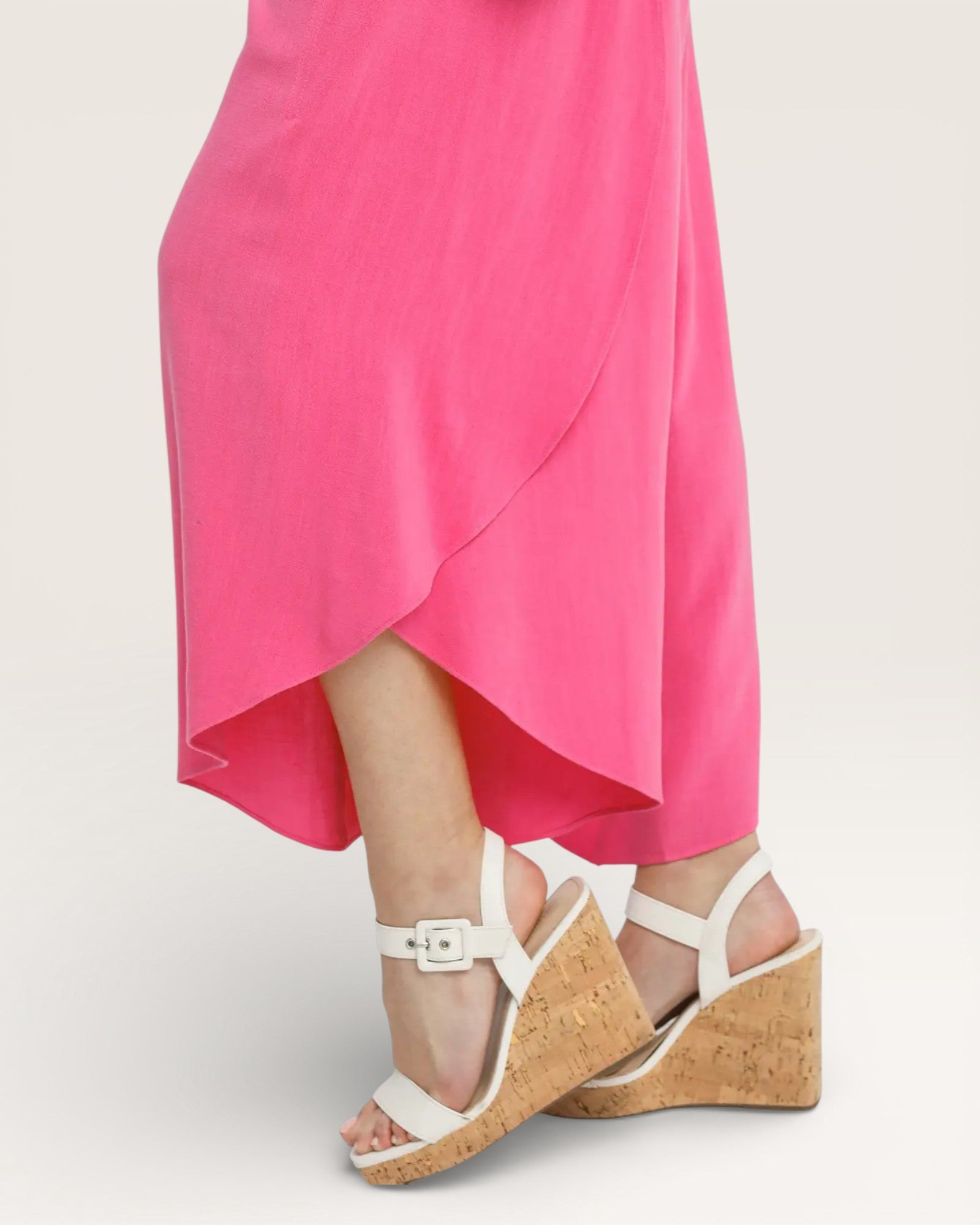 Person wearing a bright pink dress with white wedge sandals on a light gray background
