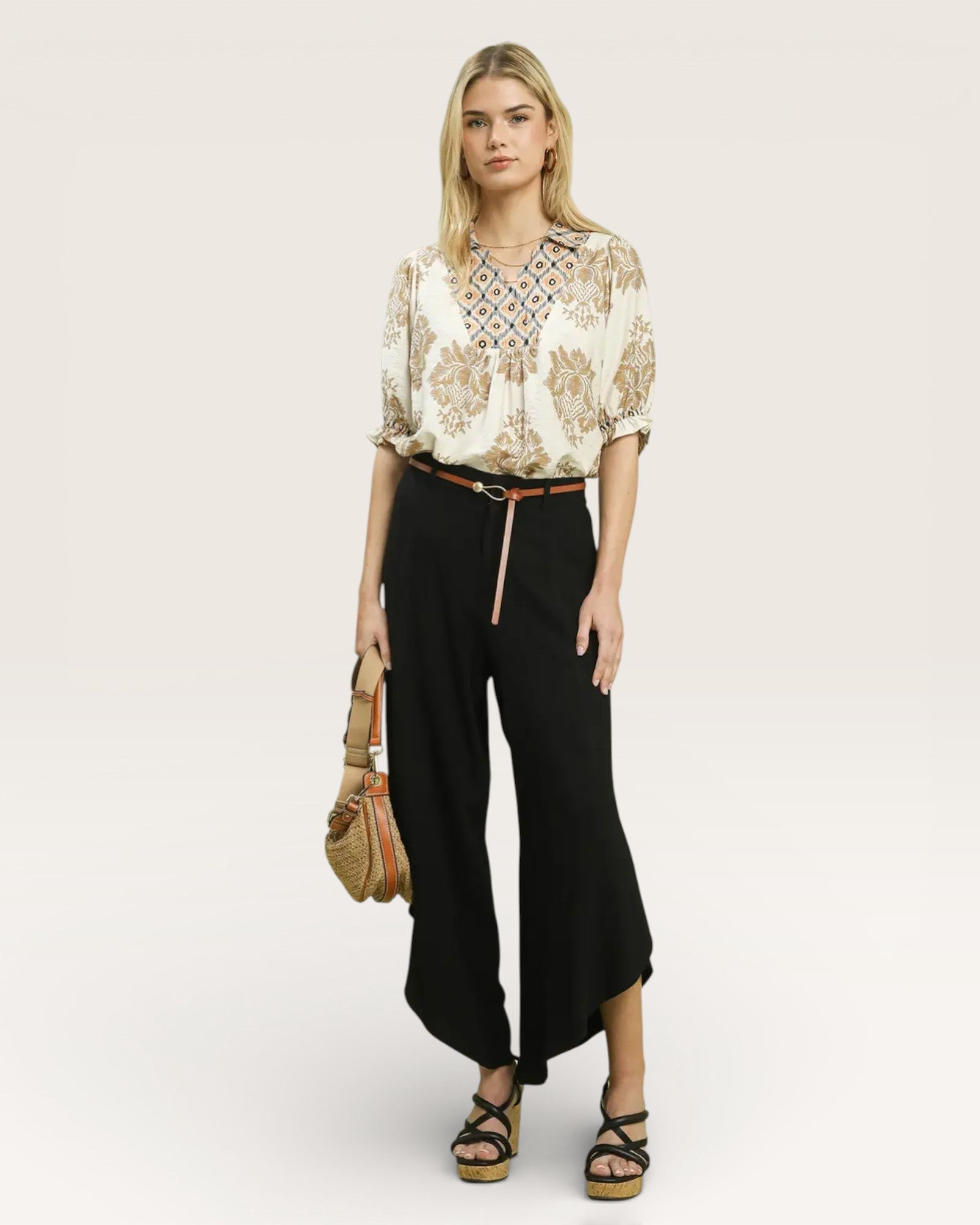 Woman wearing a floral blouse and black pants with a beige background
