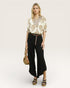Woman wearing a floral blouse and black pants with a beige background