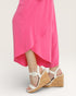 Person wearing a bright pink dress with white wedge sandals on a light gray background