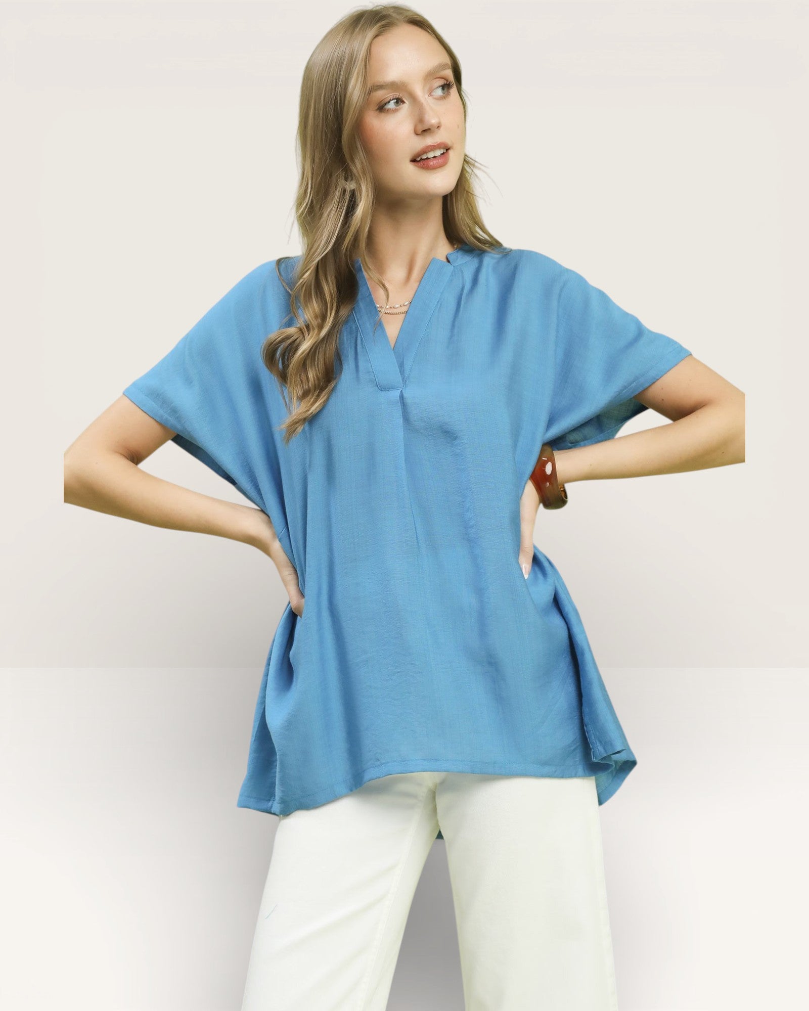 Woman wearing a blue top and white pants on a plain background