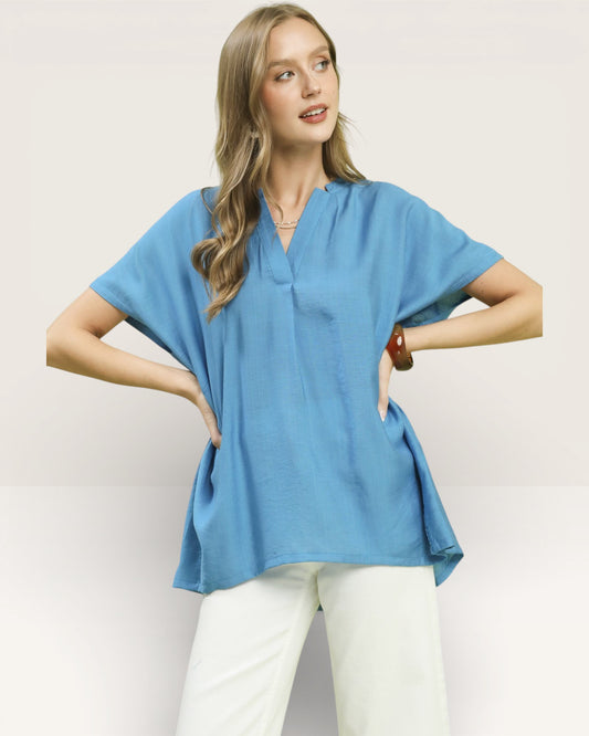 Woman wearing a blue top and white pants on a plain background