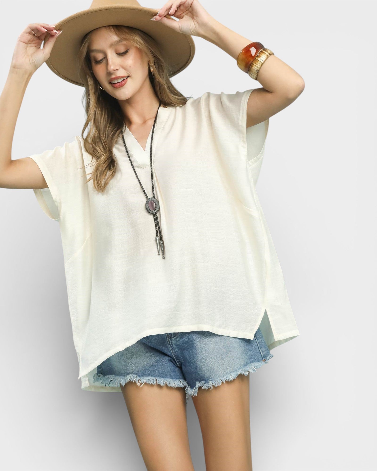 Woman wearing a white blouse, denim shorts, and a wide-brimmed hat on a plain background