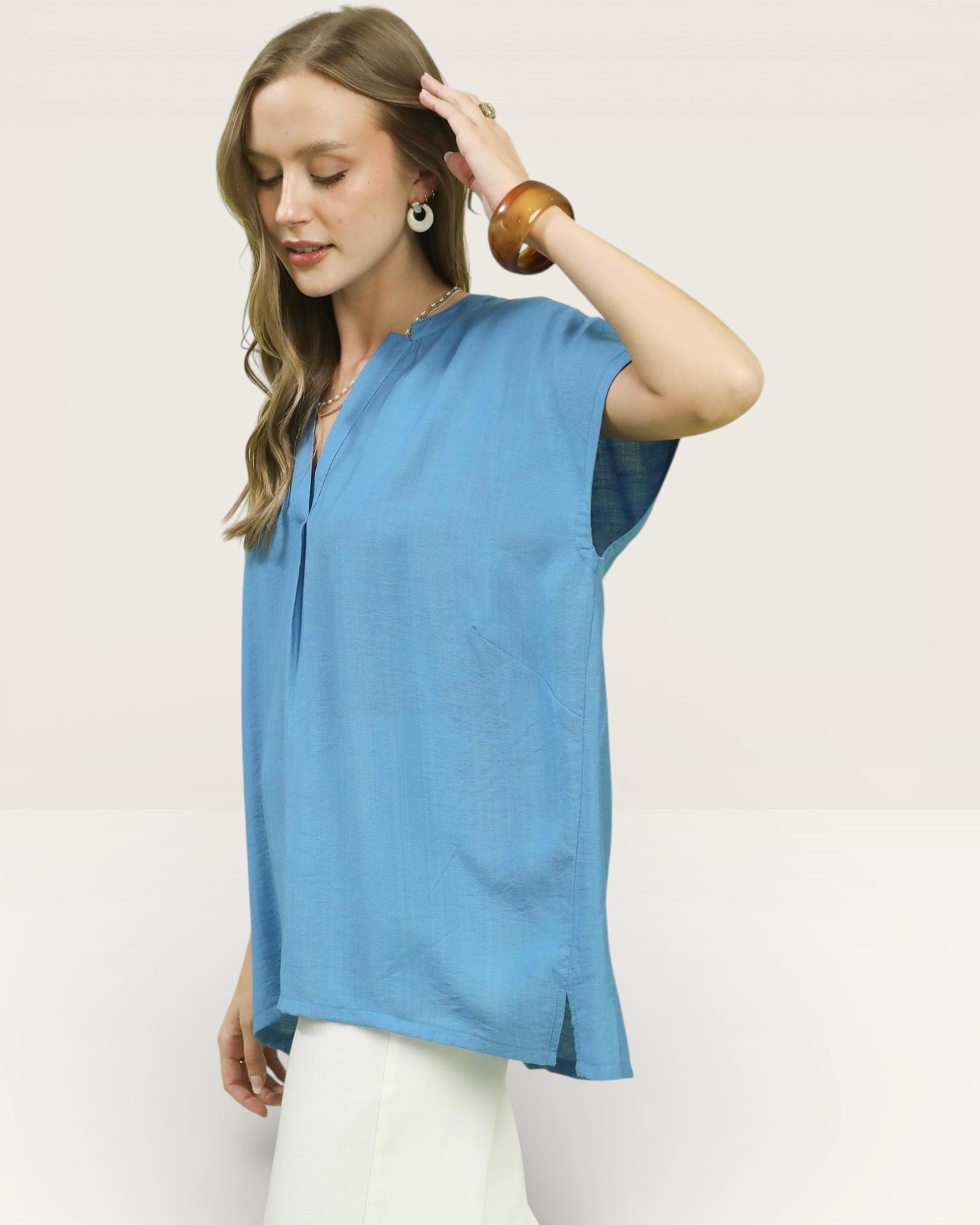 Woman wearing a blue top and white pants against a plain background