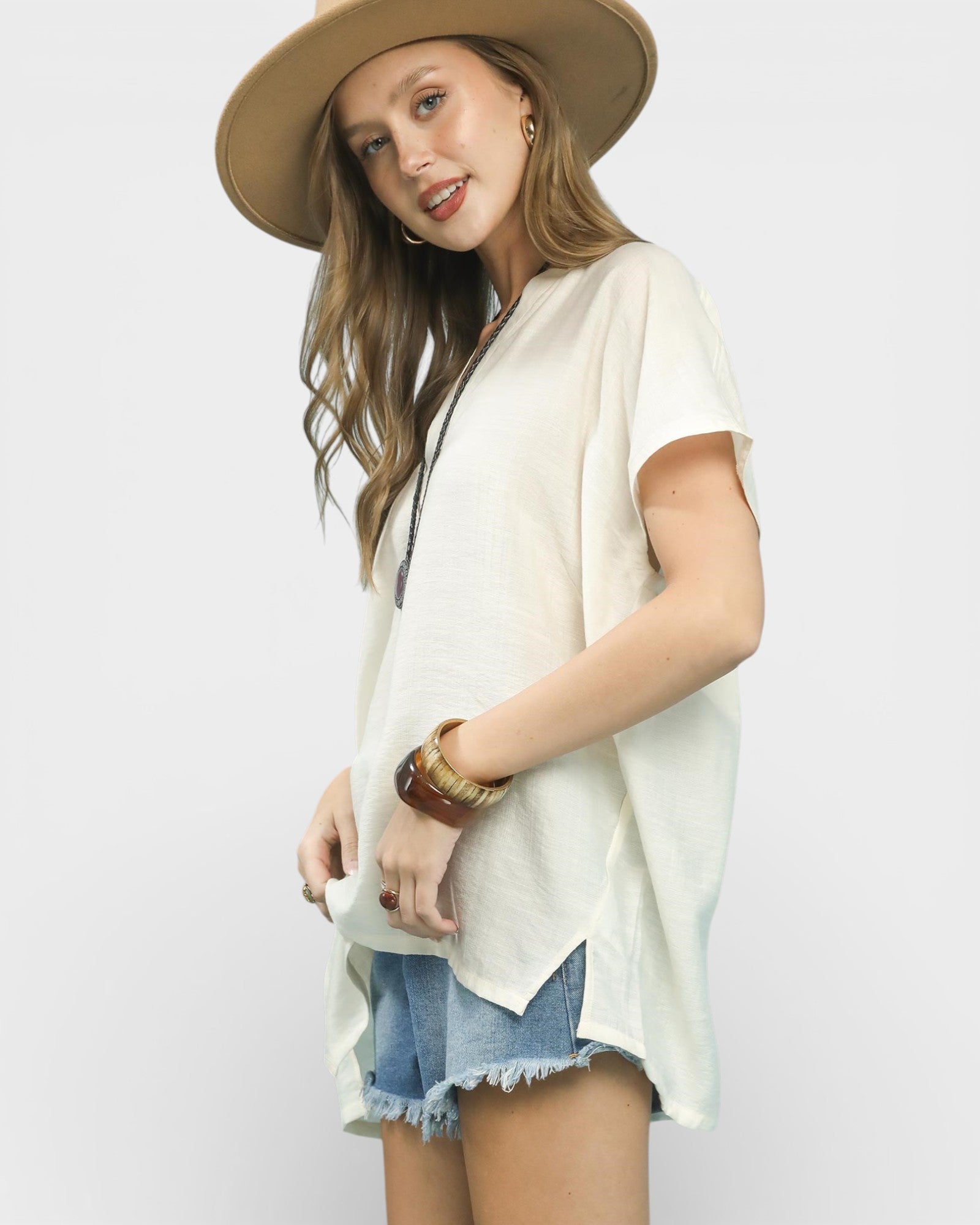 Woman wearing a beige hat, white top, and denim shorts on a plain background