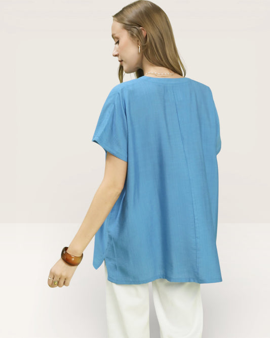 Woman wearing a blue top and white pants on a plain background