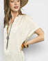 Woman wearing a beige outfit with a hat and jewelry on a light gray background