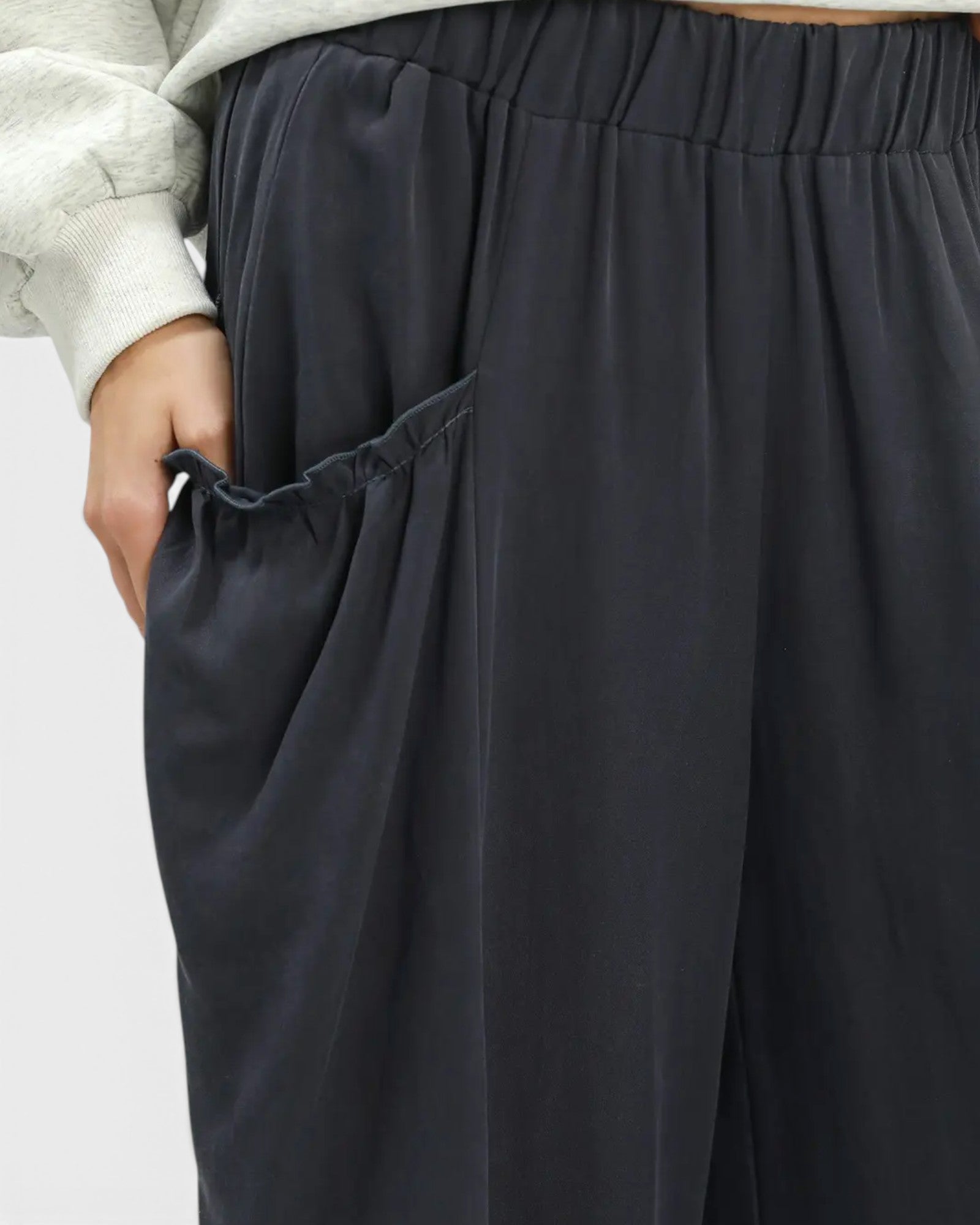Close-up of a person wearing dark charcoal wide-leg pants with an elastic waistband and a side pocket, paired with a light gray sweatshirt sleeve.