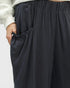Close-up of a person wearing dark charcoal wide-leg pants with an elastic waistband and a side pocket, paired with a light gray sweatshirt sleeve.