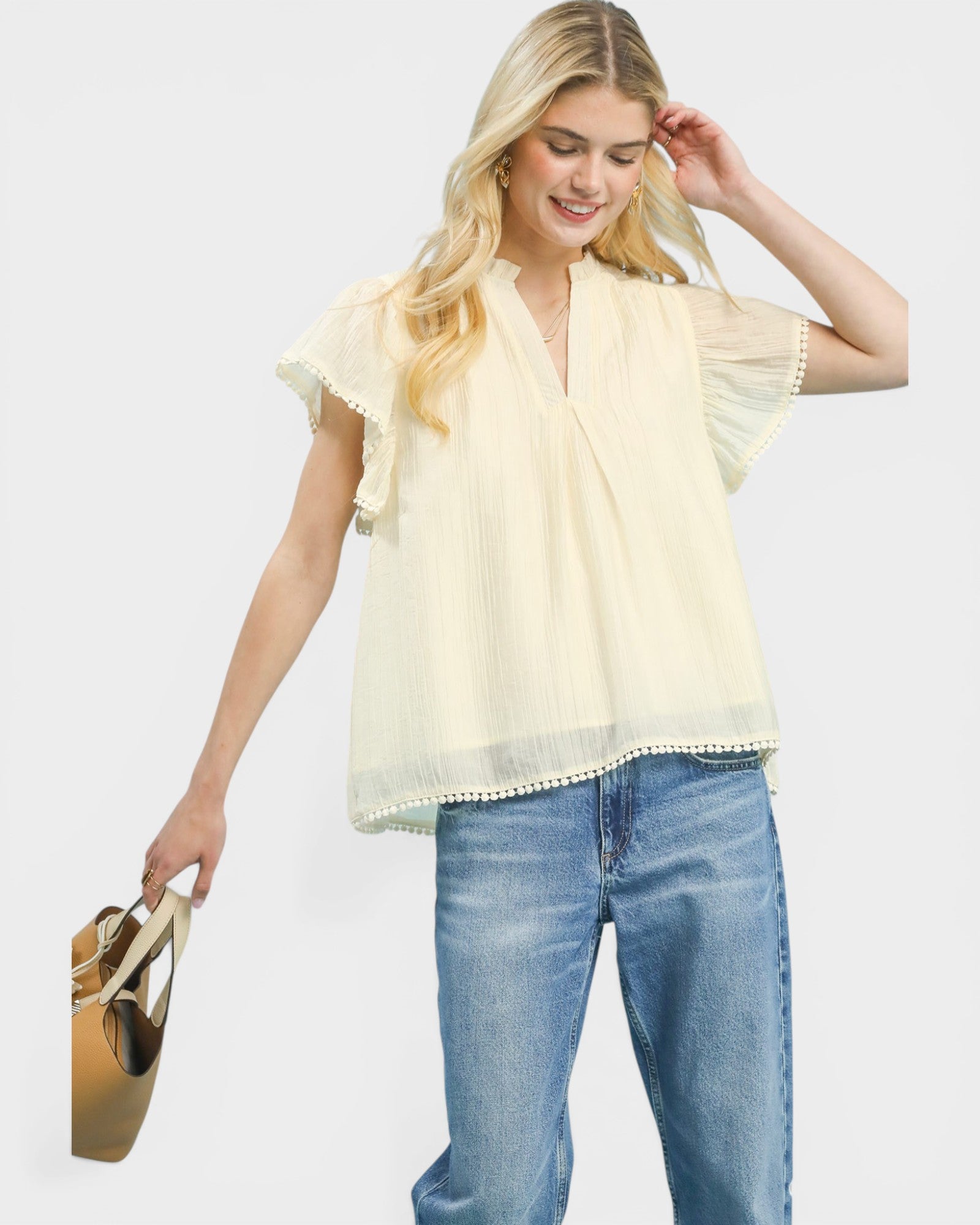 Woman wearing a light yellow blouse and blue jeans, holding a bag on a white background