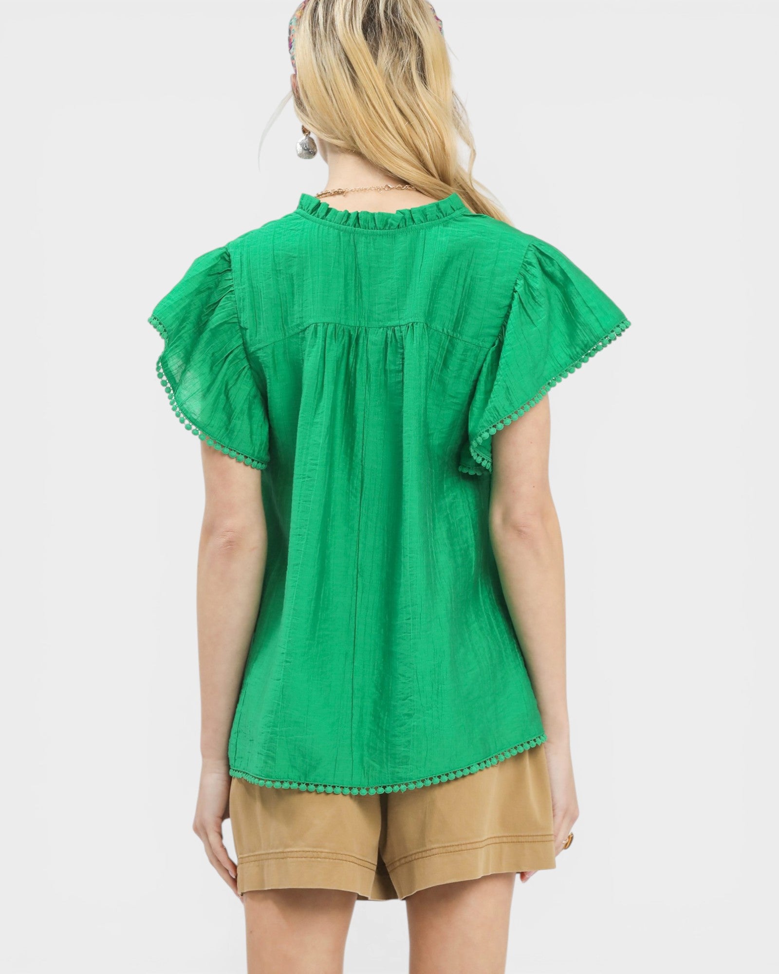 Green blouse with ruffled sleeves worn by a person on a white background