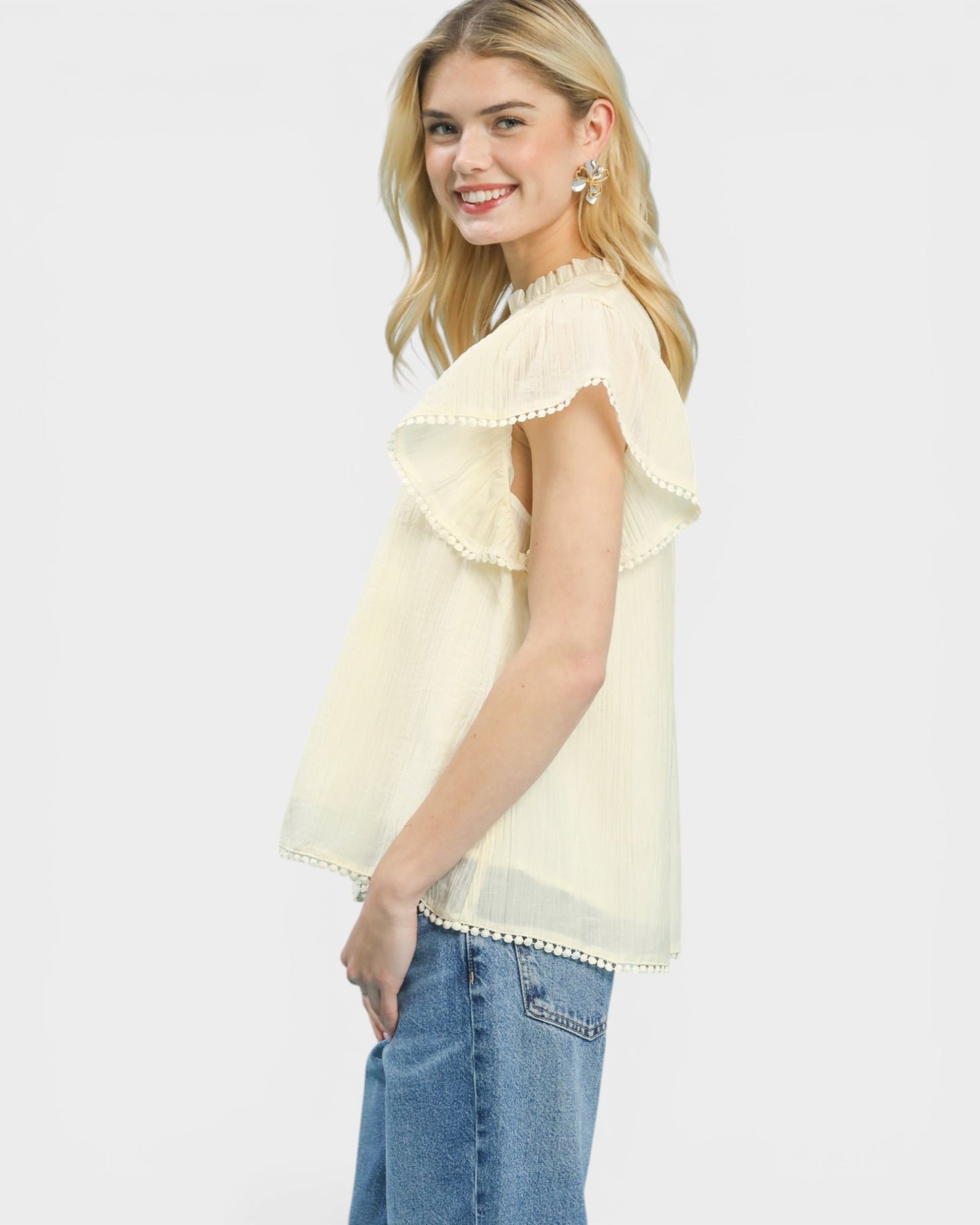 Woman wearing a light yellow blouse with ruffled sleeves and blue jeans on a white background