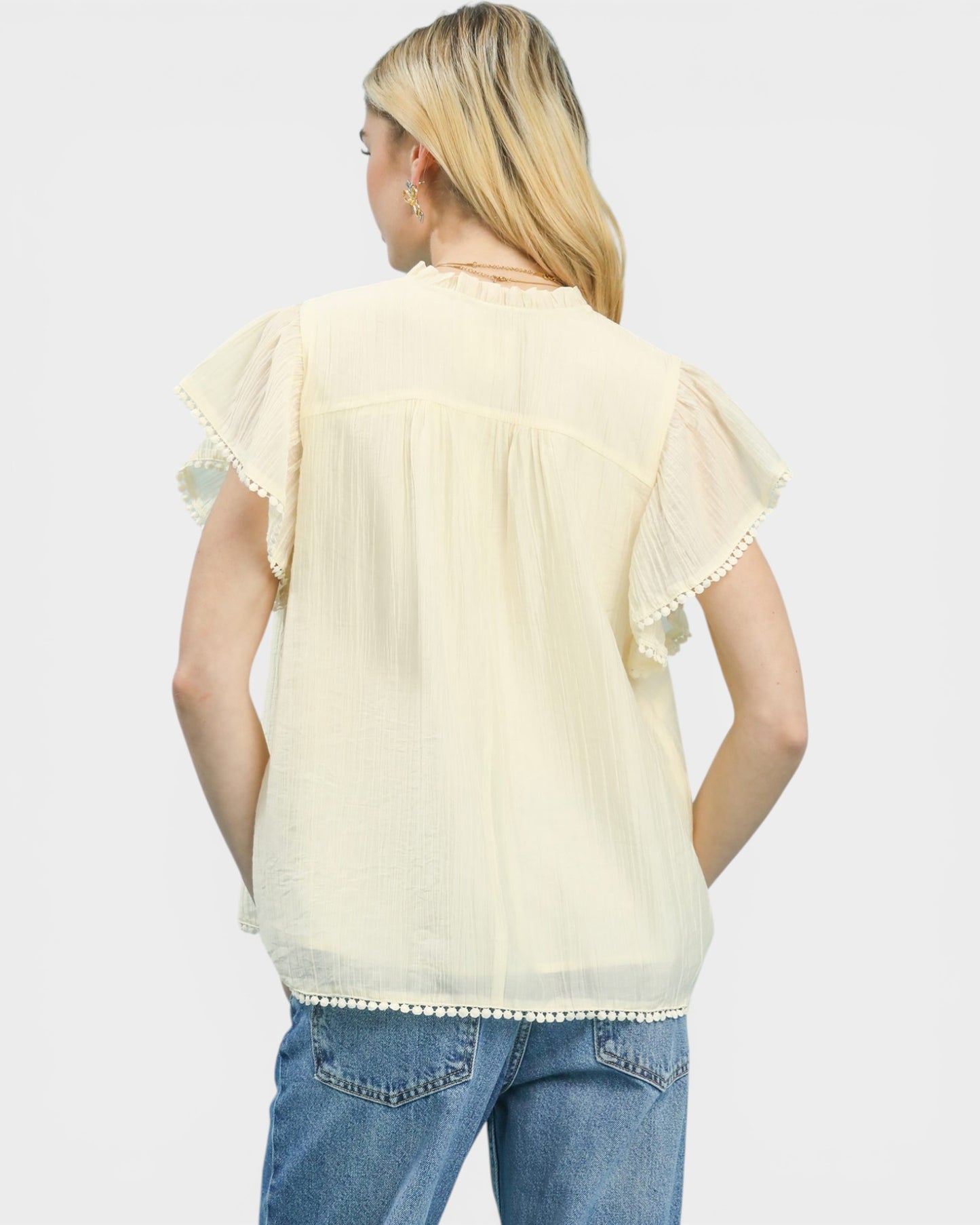 Woman wearing a light yellow blouse with ruffled sleeves and blue jeans on a white background