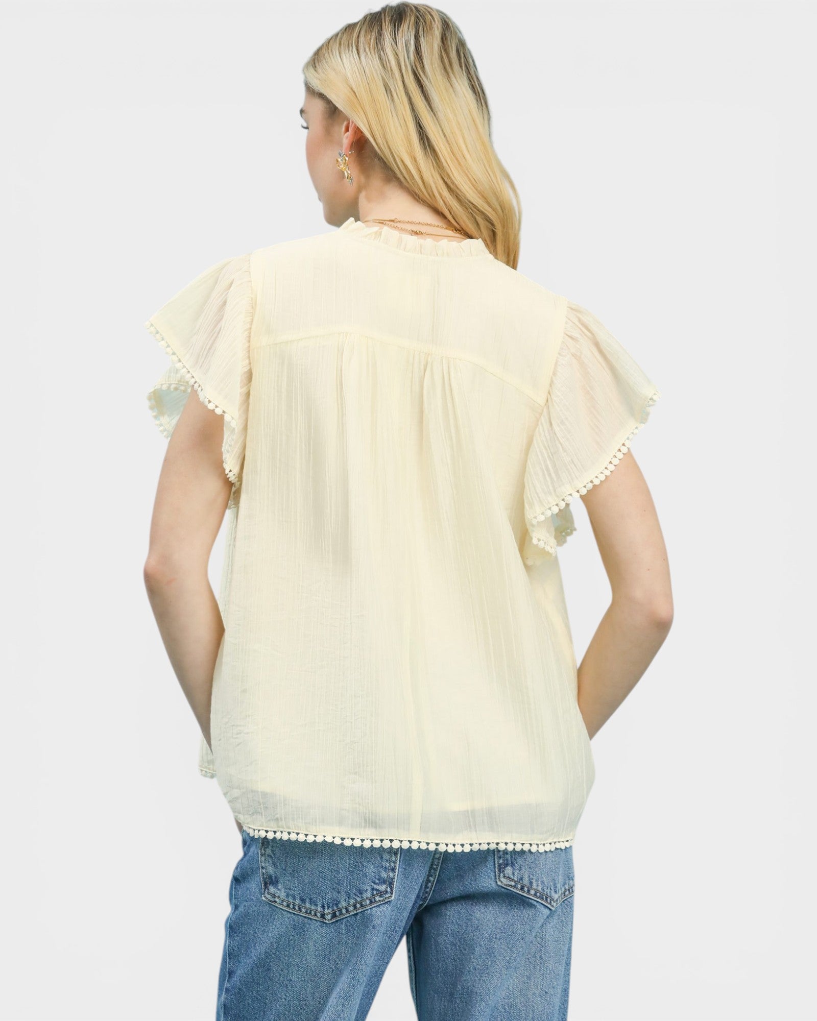 Woman wearing a light yellow blouse with ruffled sleeves and blue jeans on a white background