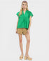 Woman wearing a green top and beige shorts on a white background