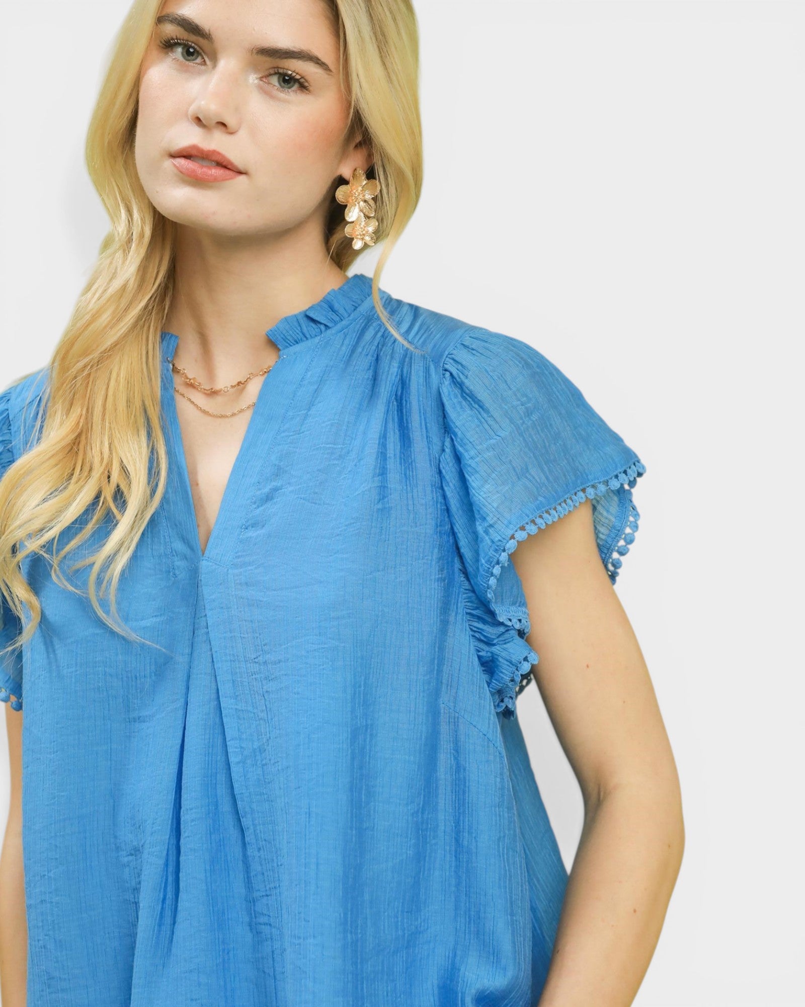 Woman wearing a blue blouse with ruffled sleeves on a plain background