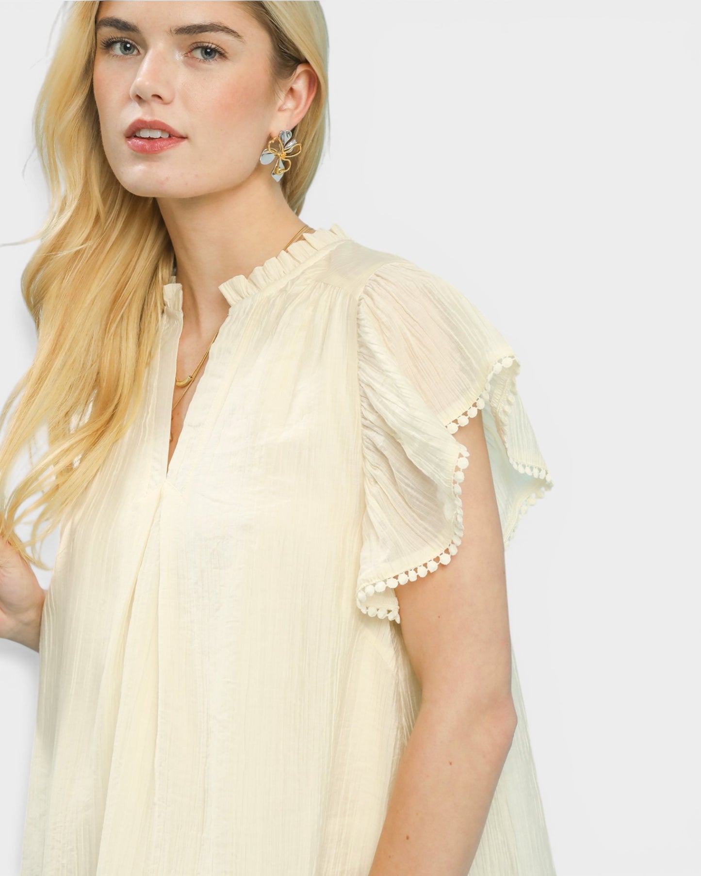 Woman wearing a light yellow blouse with ruffled sleeves against a plain background