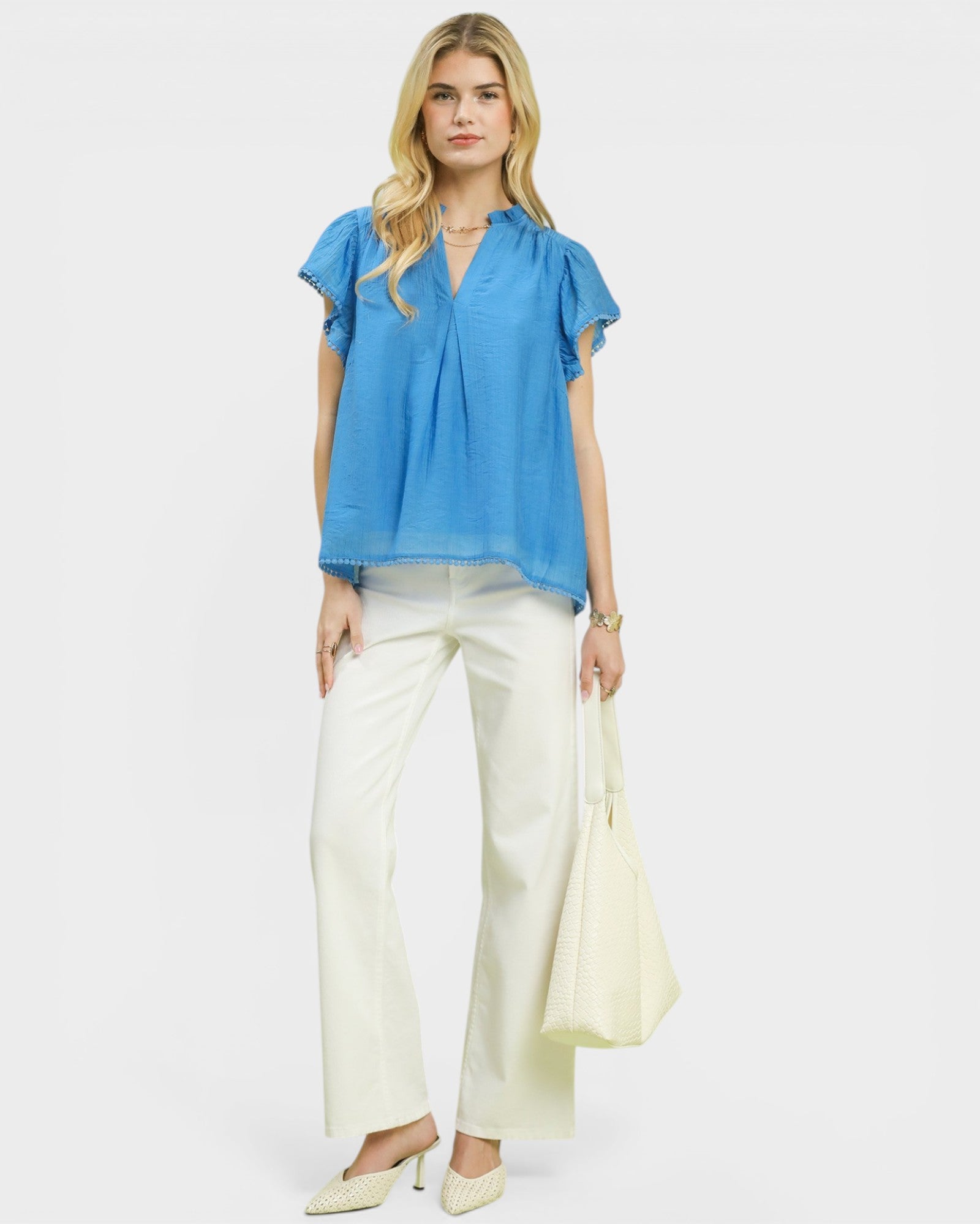 Woman wearing a blue blouse and white pants on a plain background