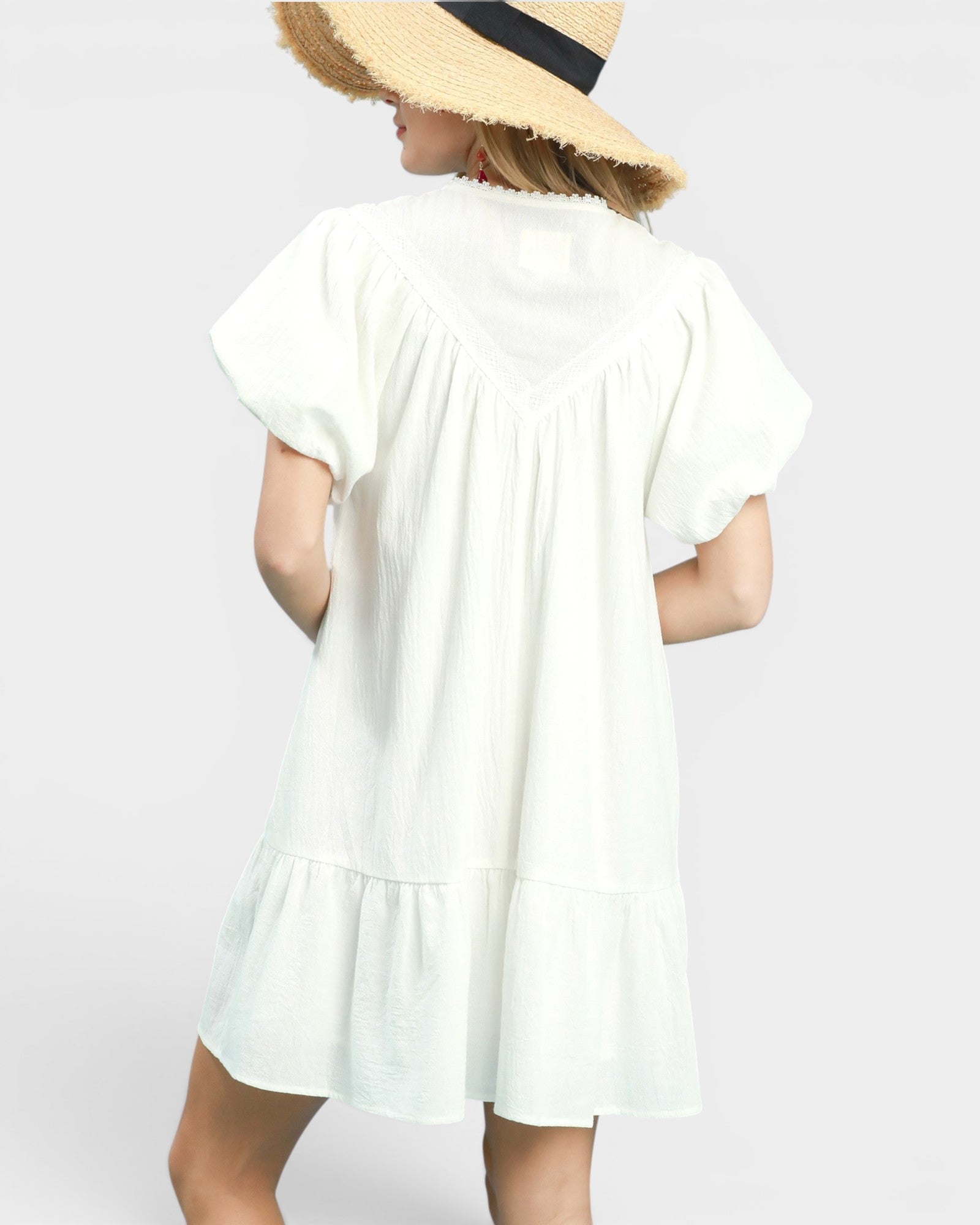 Person wearing a white dress with a straw hat on a plain background