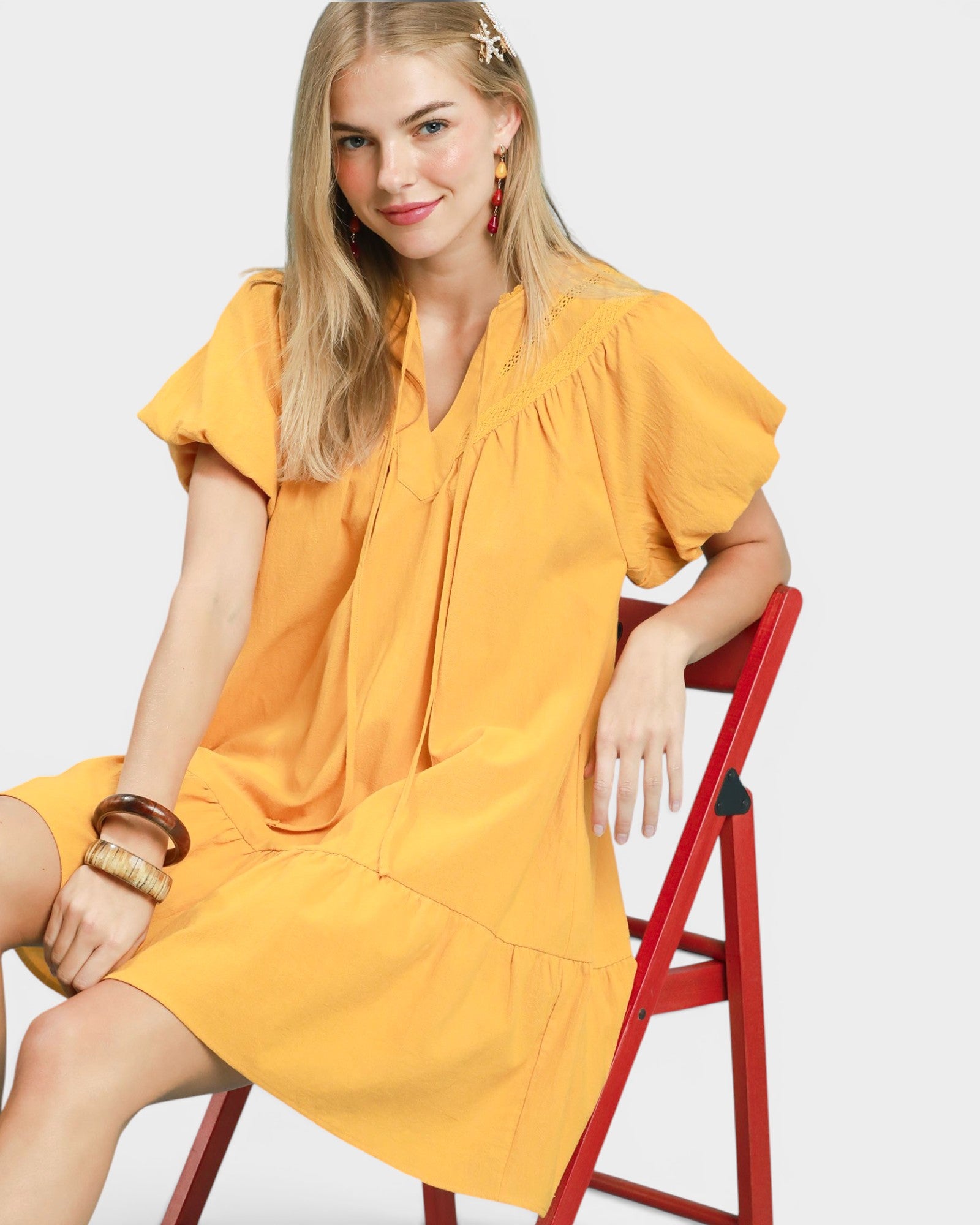 Woman in a yellow dress sitting on a red chair against a white background